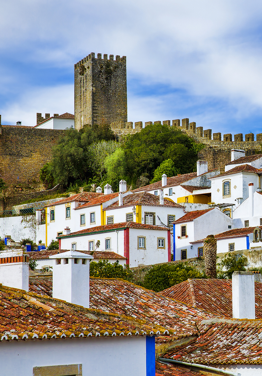 Vila de Óbidos, casas blancas con rayas amarillas, azules y rojas, con el castillo de fondo