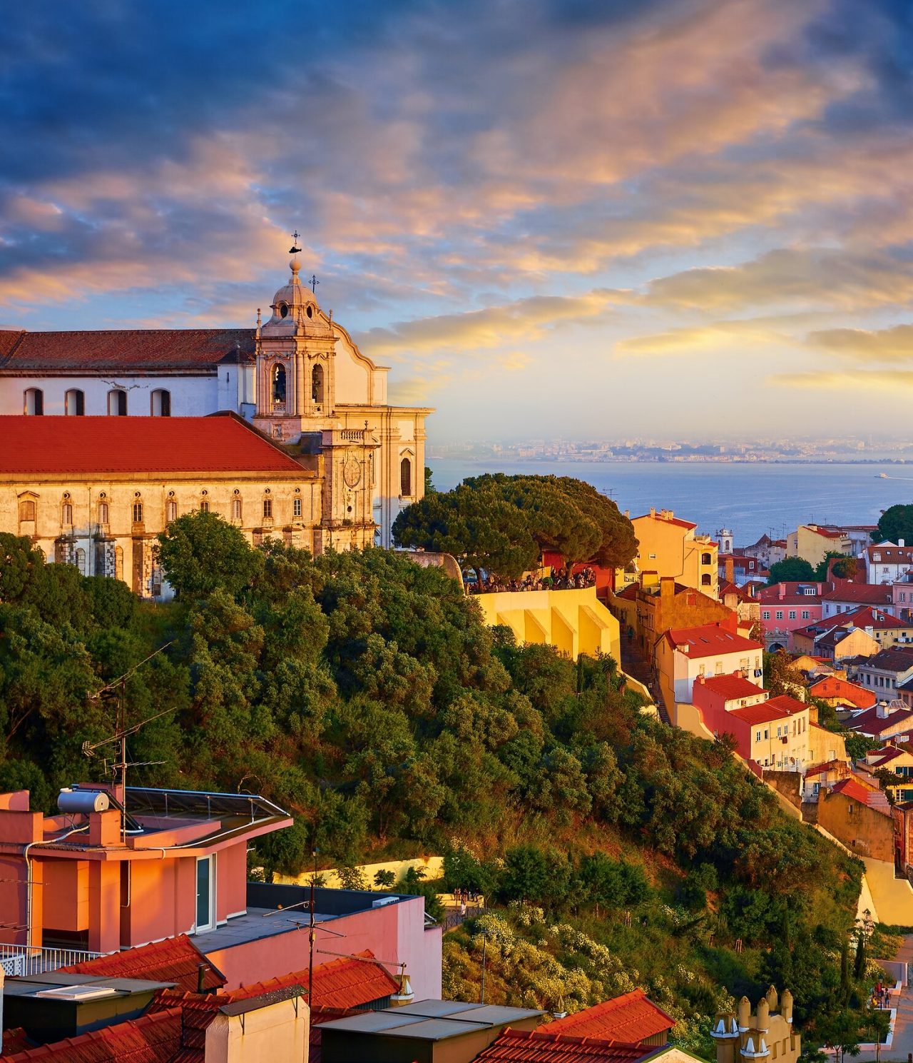 Explora Hoteles en Lisboa con vistas a una iglesia histórica sobre la colina y tejados junto al río al atardecer
