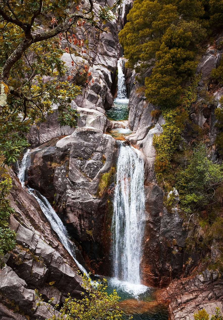 Agua cayendo de una cascada rocosa, rodeada de vegetación en el Parque Nacional Peneda-Gerês