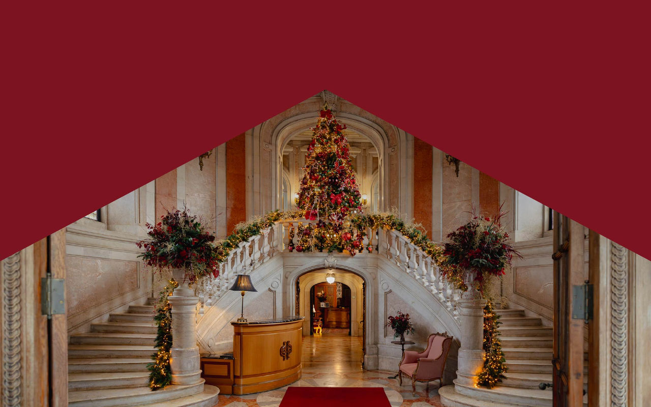 Vestíbulo con escalera de mármol decorada con guirnaldas navideñas y gran árbol iluminado al fondo