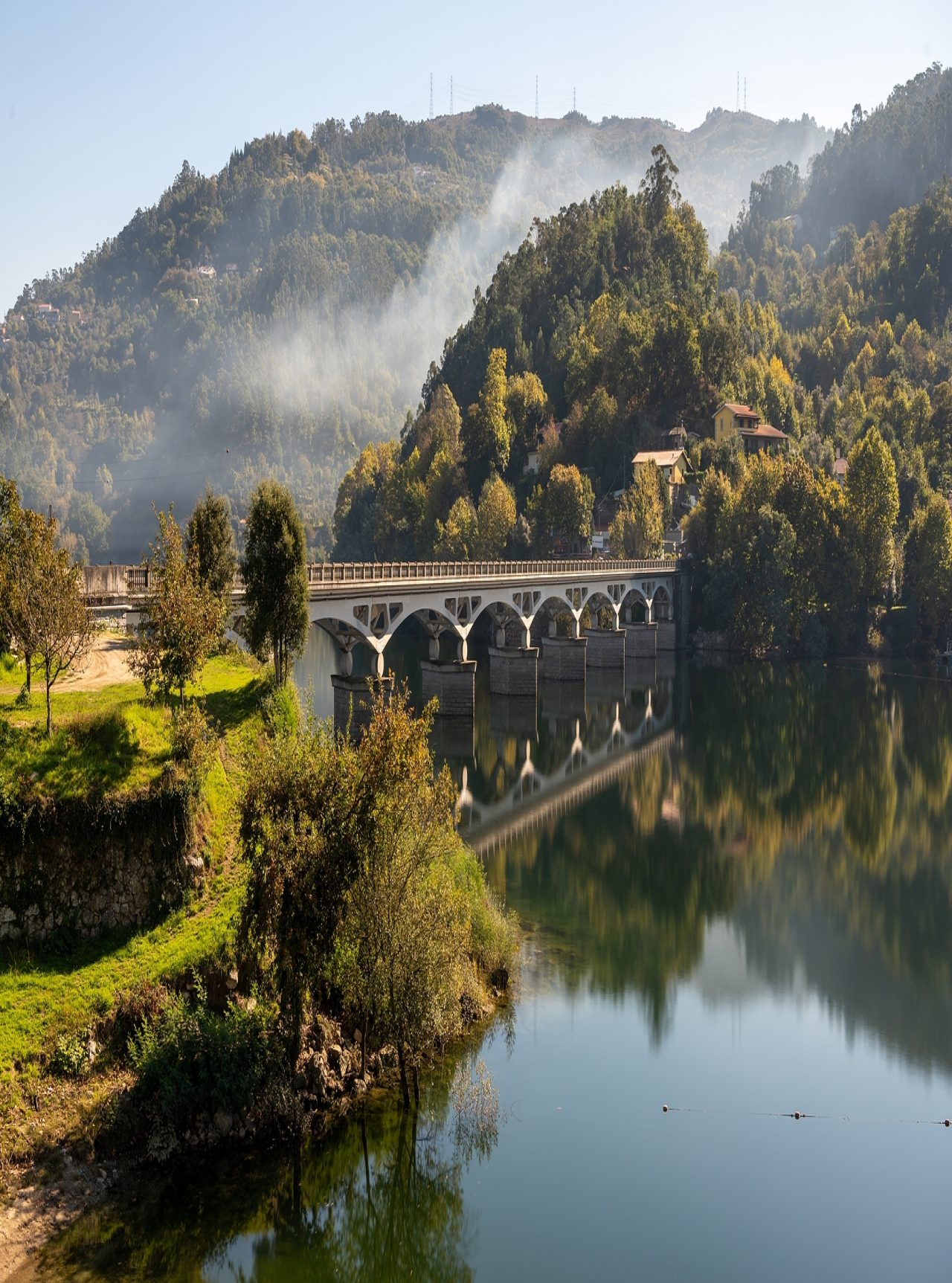 Paisagem do norte de Portugal com uma ponte de pedra sobre um rio, cercada por colinas verde