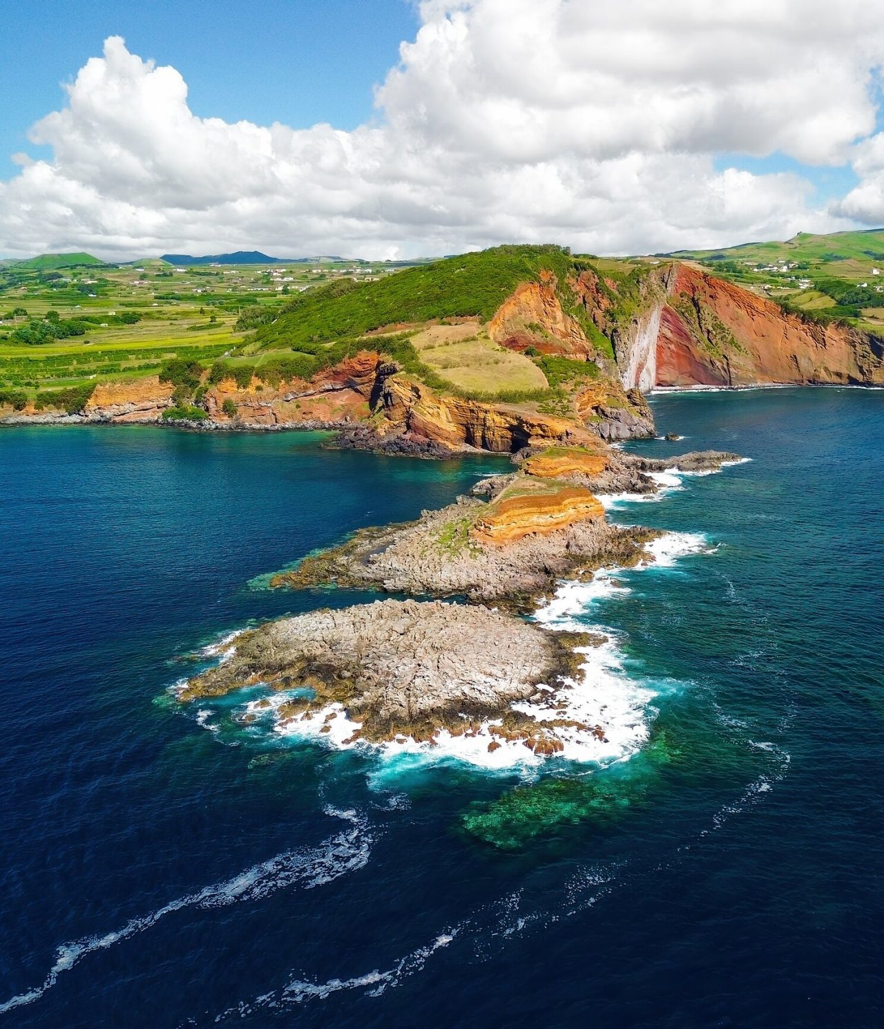 Vista aérea de formações rochosas vulcânicas esculpidas pelo mar, rodeadas pelo oceano e vegetação verde