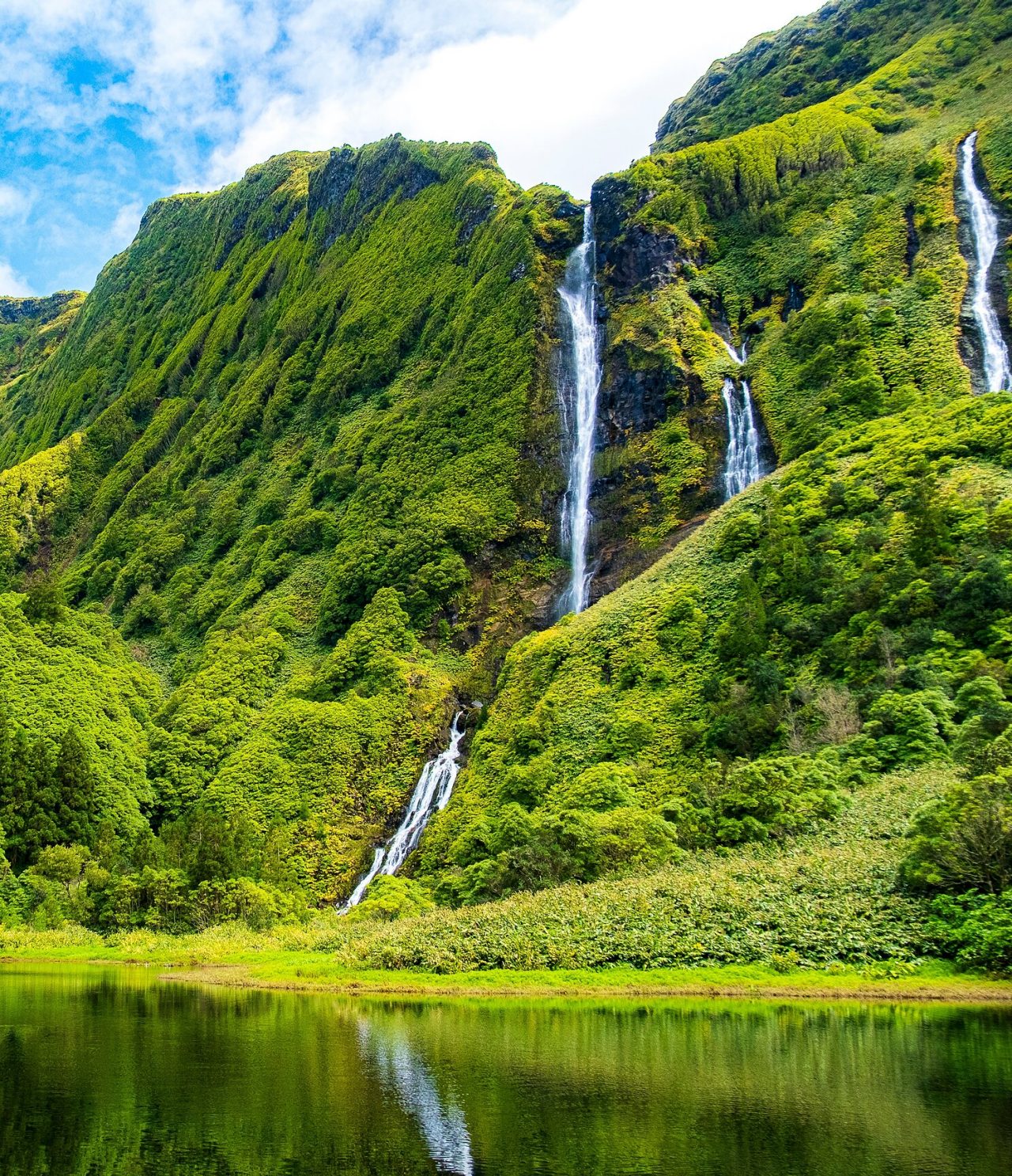 Cascata deslumbrante rodeada por montanhas de vegetação verdejante na ilha das Flores, nos Açores