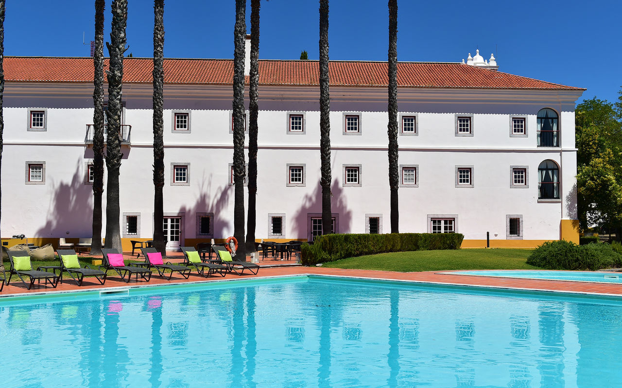 Piscina exterior da Pousada Convento Beja, um hotel histórico no Alentejo, com várias espreguiçadeiras com almofadas