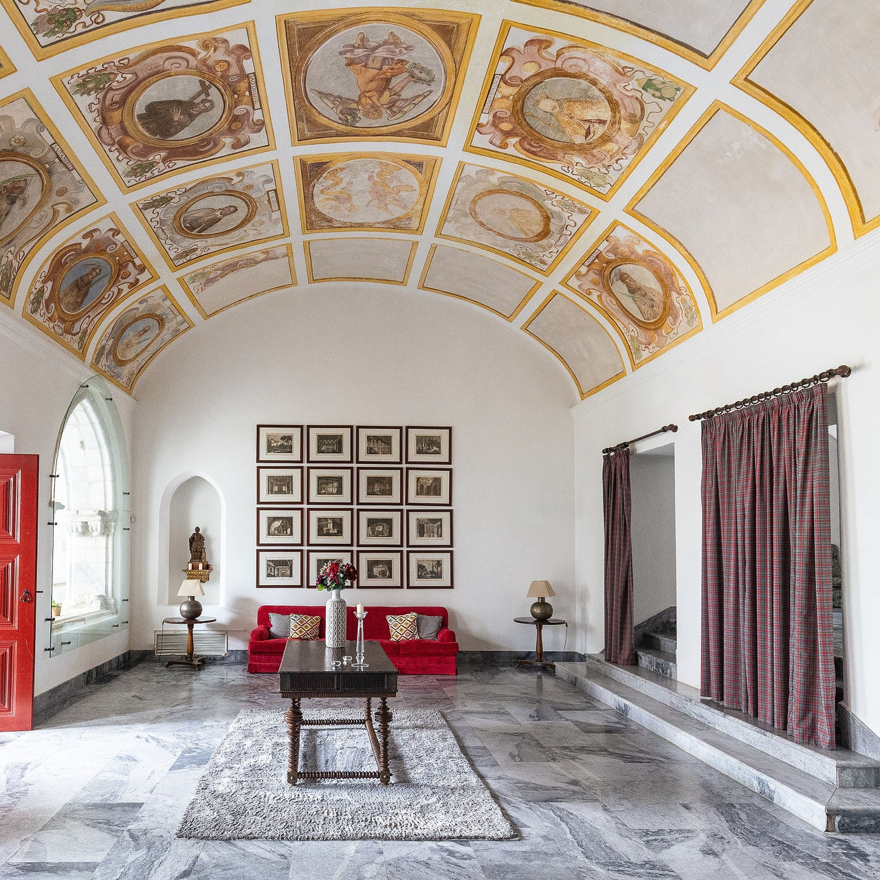 Hall da Pousada Convento Beja, com teto pintado com grande detalhe, uma mesa no centro e um sofá no fundo