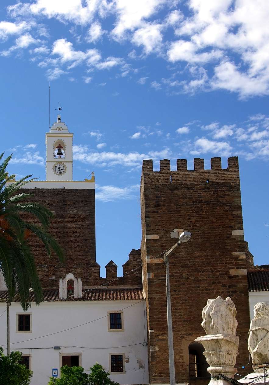 Vista para o castelo de Alandroal, com a sua torre em pedra e um sino no topo, com palmeiras à frente