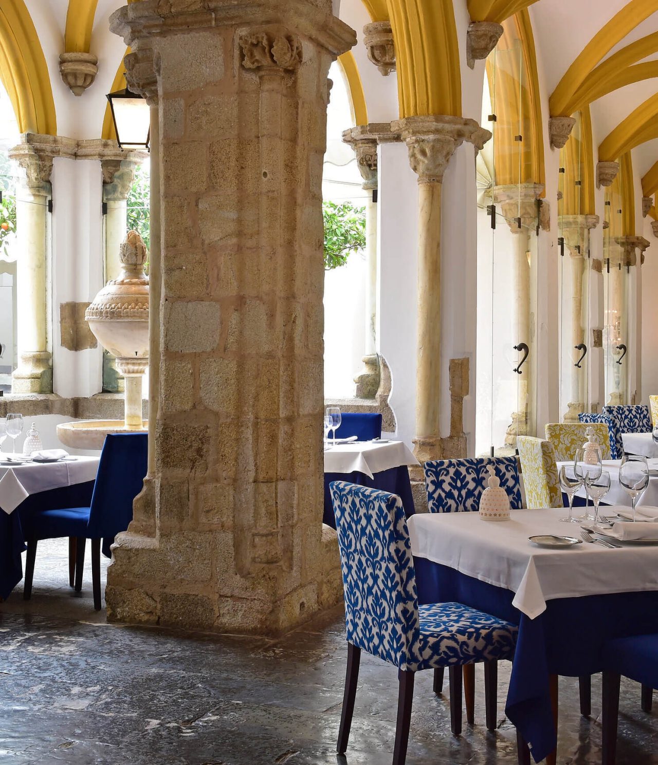 O restaurante Loios, do Hotel Histórico em Évora tem colunas de pedra, arcos amarelos e uma fonte em pedra