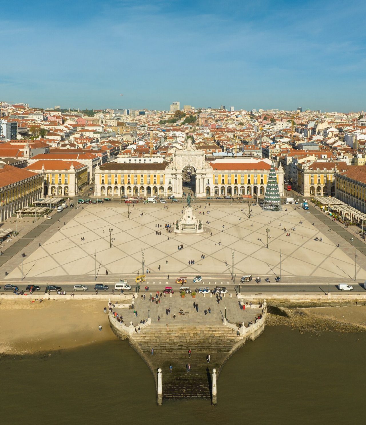 Vista aérea da Praça do Comércio, em Lisboa, com o rio Tejo à frente, a estátua no meio e uma árvore de natal