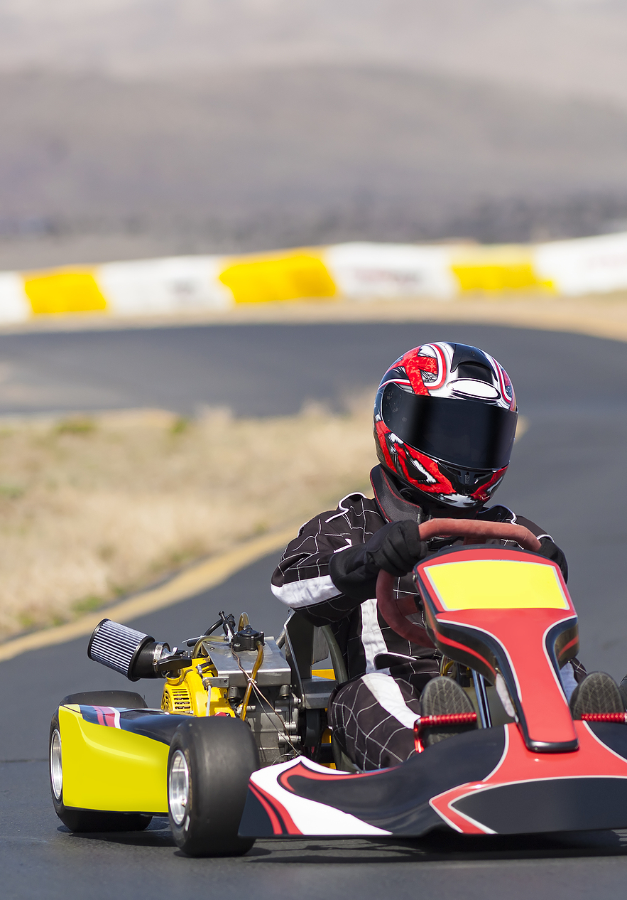 Circuito de Kart, com um piloto com macacão de corrida preto e branco e um capacete vermelho e preto