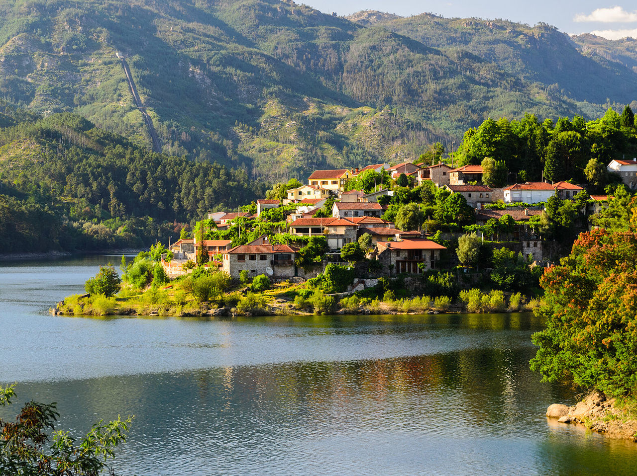 Pequena vila com telhados vermelhos à beira do rio douro, cercada por uma paisagem verde