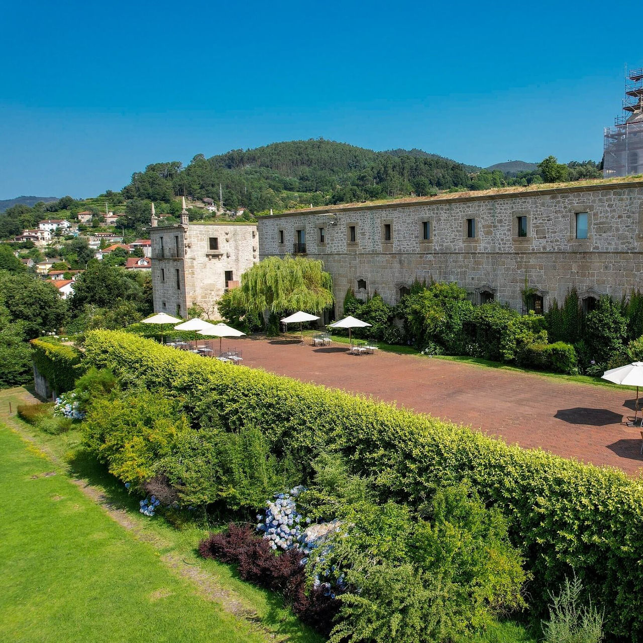 Vista do exterior da Pousada Mosteiro Amares, um hotel histórico no Gerês, com jardins e chapéus de sol à volta