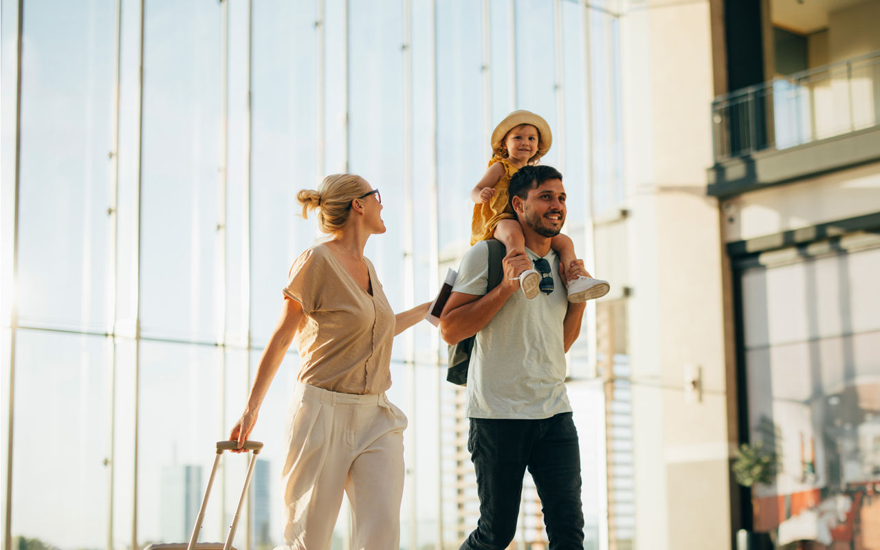 Família sorridente com malas de viagem, chega a um hotel do Pestana Hotel Group num dia de sol
