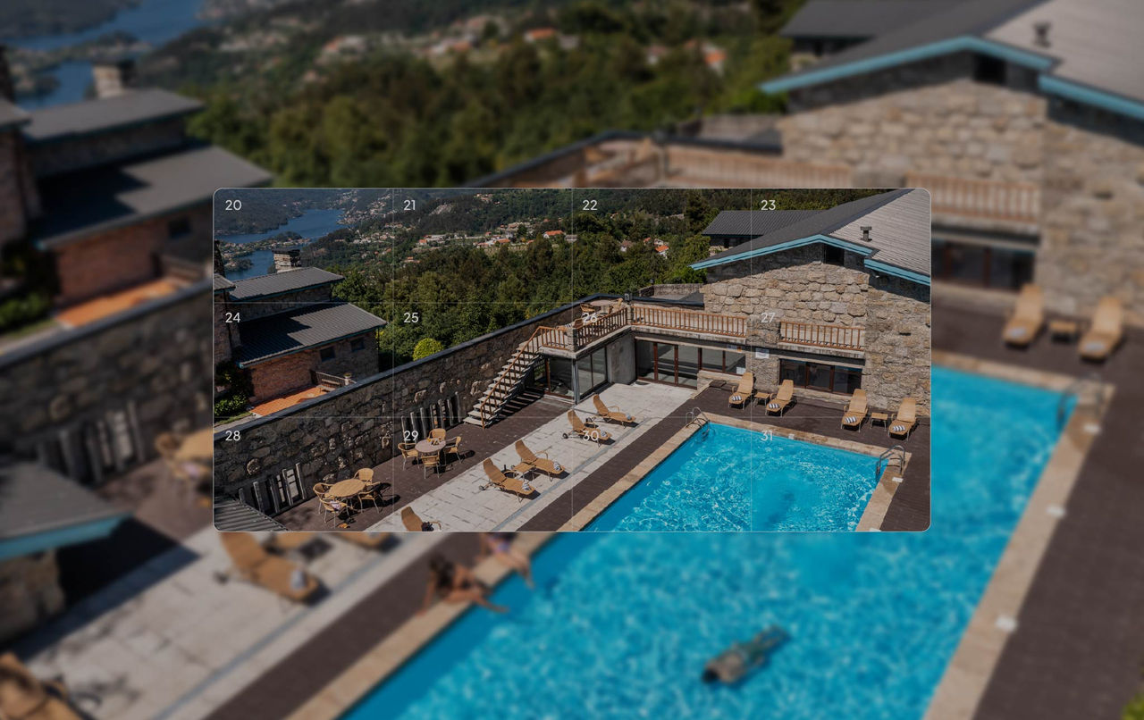 Piscina ao ar livre cercada por construções de pedra, mesas e espreguiçadeiras com vista verde das montanhas