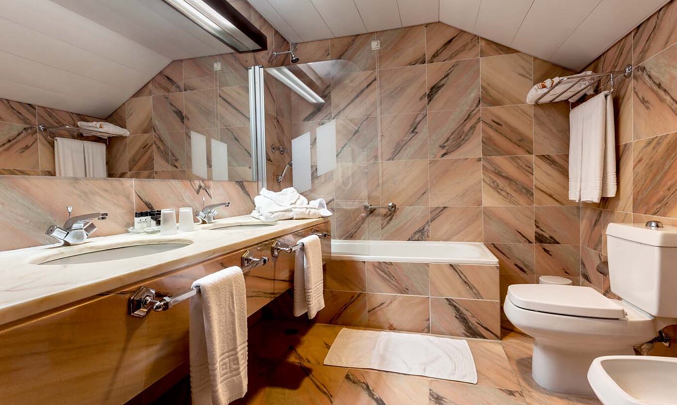 Die Standard Suite der Pousada Castelo Alvito hat ein Badezimmer aus Marmor mit Waschbecken Toilette und Badewanne mit Dusche