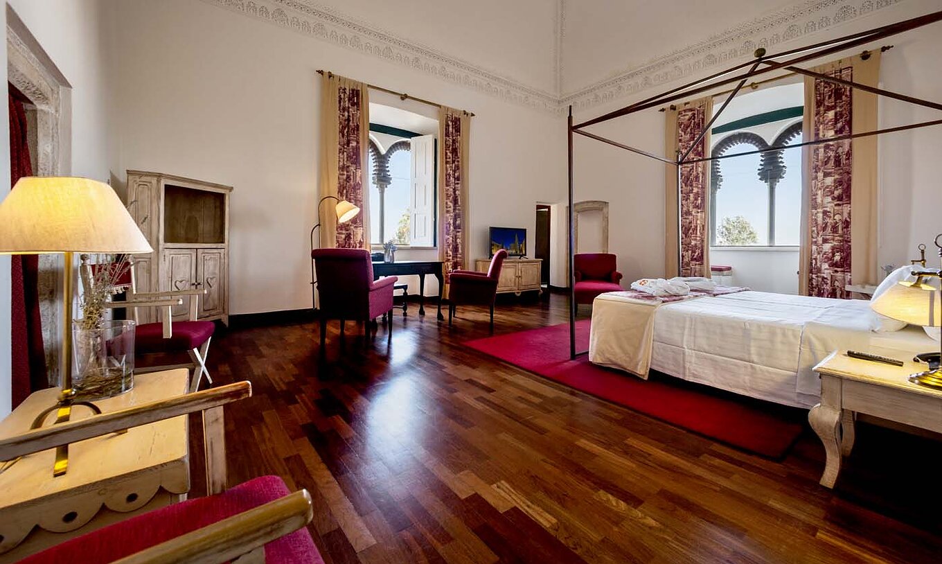 Die Spezial Suite der Pousada Castelo Alvito hat zwei Betten einen Nachttisch und zwei Fenster mit Blick auf das Dorf