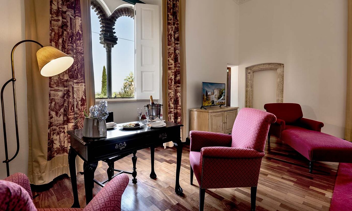 Die Spezial Suite der Pousada Castelo Alvito hat einen Tisch mit einer Flasche Champagner und ein Fenster in Bögen