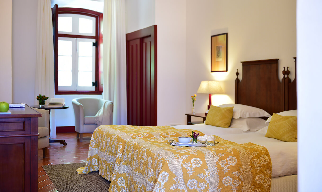 Das Familienzimmer der Pousada Convento Beja hat zwei Betten mit gelber Bettdecke ein Fenster und Schränke