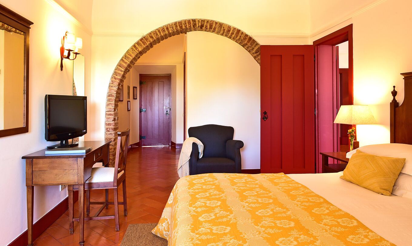 Die Standard Suite der Pousada Convento Beja hat ein Doppelbett mit gelber Bettdecke einen Fernseher und einen Sessel