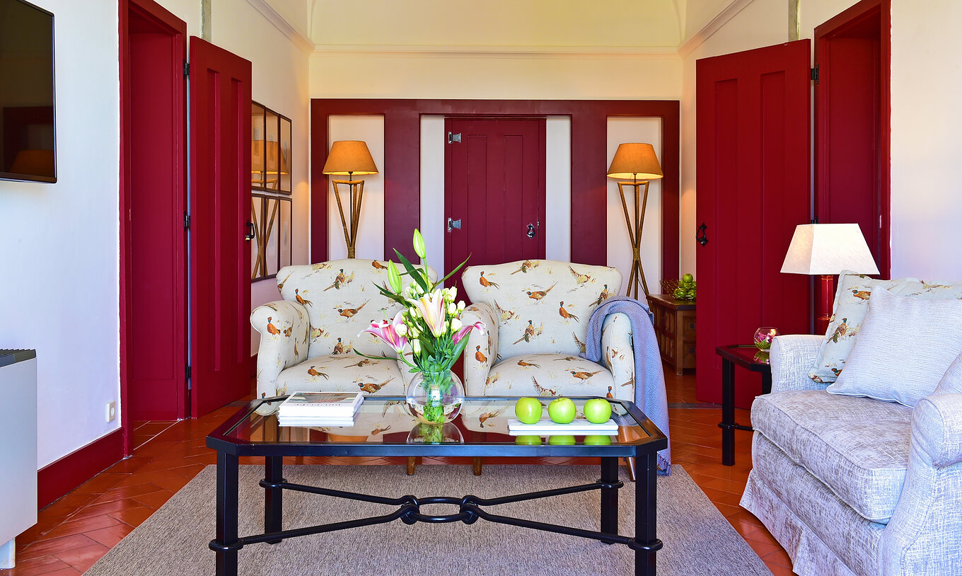 Die Standard Suite der Pousada Convento Beja hat ein Wohnzimmer mit einem Sofa und zwei Sesseln mit Vogelmotiv