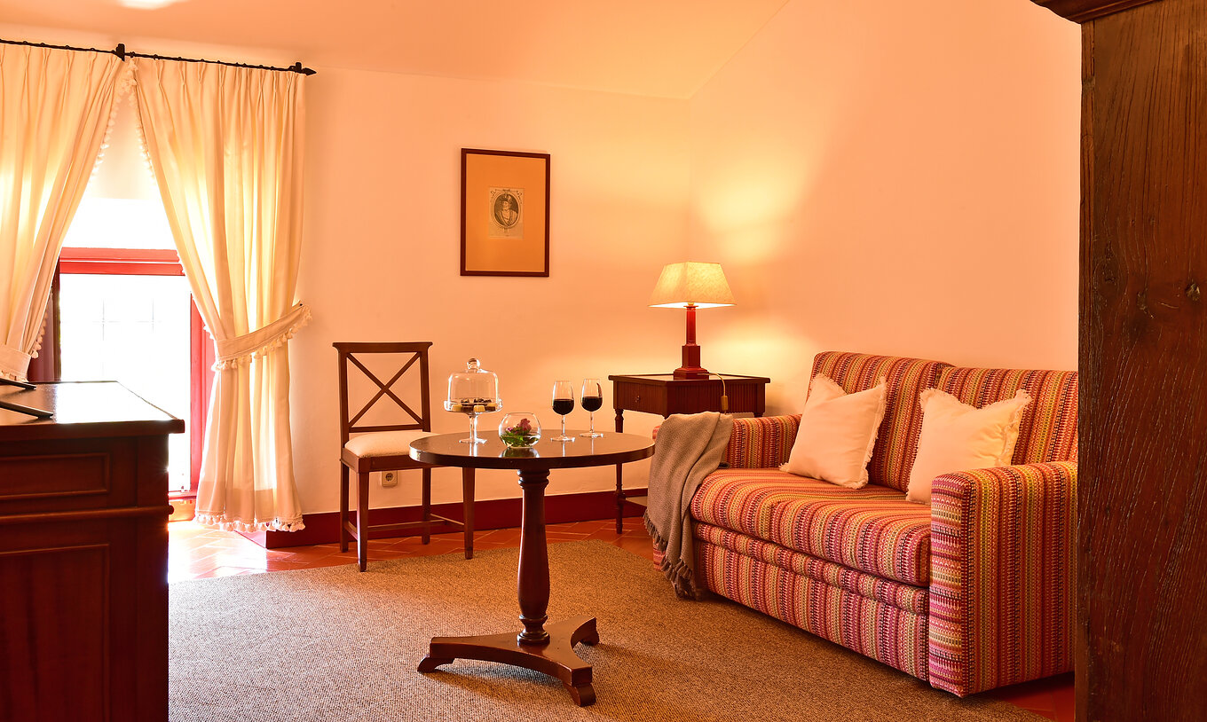 Die Spezial Suite der Pousada Convento Beja hat ein Wohnzimmer mit einem Sofa einem Beistelltisch und zwei Weingläsern
