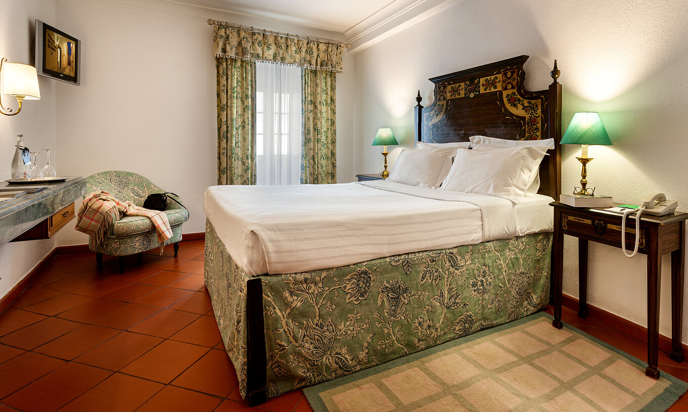 Das Klassische Zimmer der Pousada Marvão verfügt über ein Bett mit floralem Muster und einer dunkelholz Kopfteil