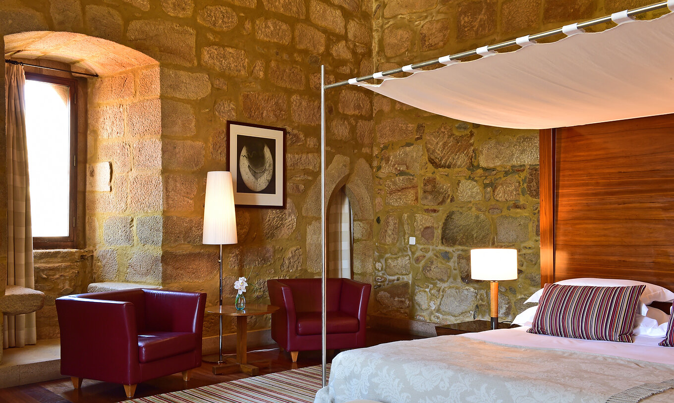 Die Master Suite der Pousada Mosteiro Crato hat Steinwände, ein Doppelbett mit Himmelbett und zwei Sessel zum Entspannen