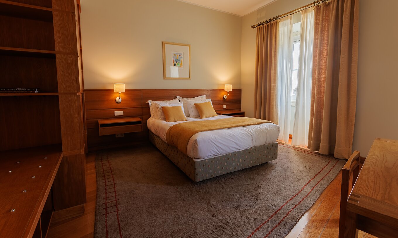 Das Einzelzimmer der Pousada Ourém hat ein Doppelbett mit gelber Bettdecke und einem Fenster daneben