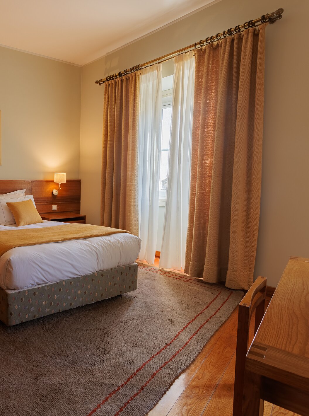 Das Einzelzimmer der Pousada Ourém hat ein Doppelbett mit gelber Bettdecke und einem Fenster daneben