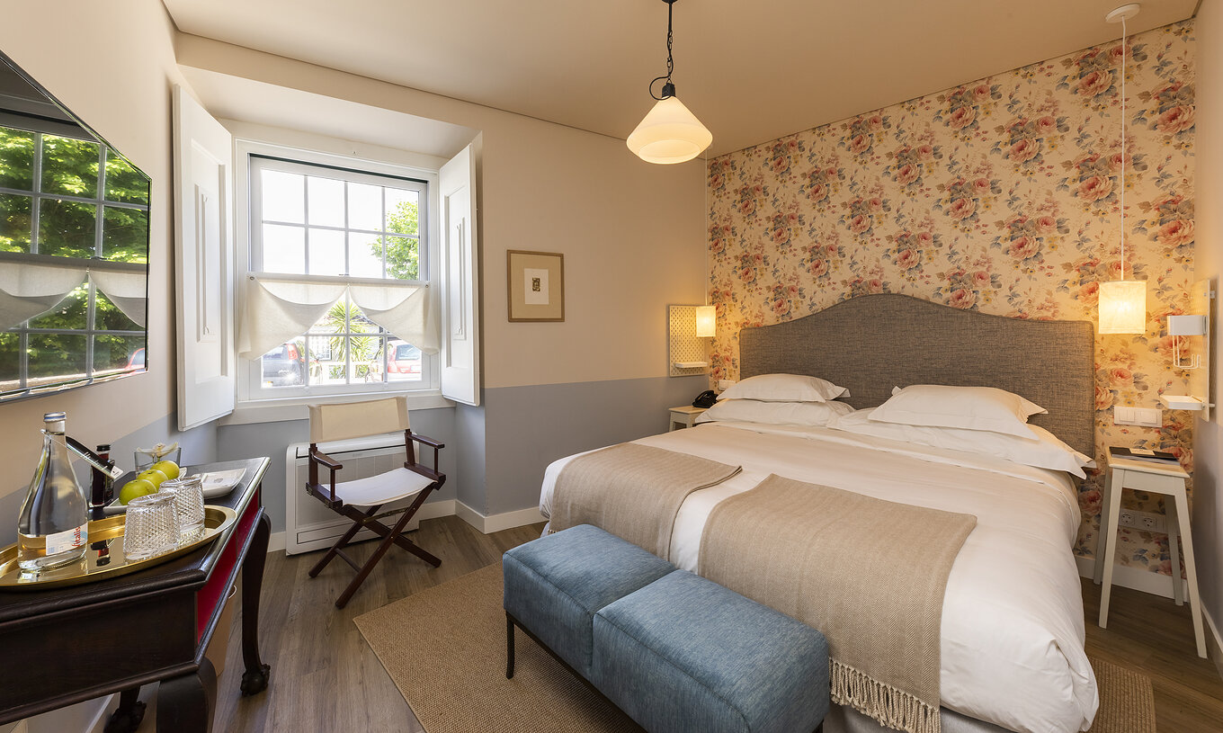 Das Classic Room der Pousada Vila Óbidos hat ein Doppelbett und eine Bank, florale Tapete und ein Fenster