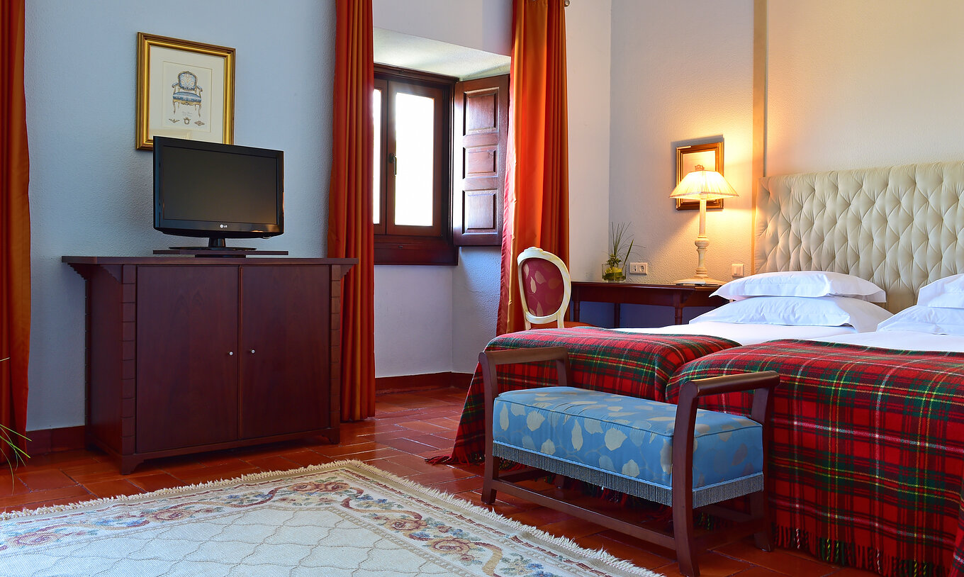 Das Klassische Zimmer der Pousada Castelo Palmela hat zwei Betten und eine Bank am Fuß des Bettes und einen Fernseher