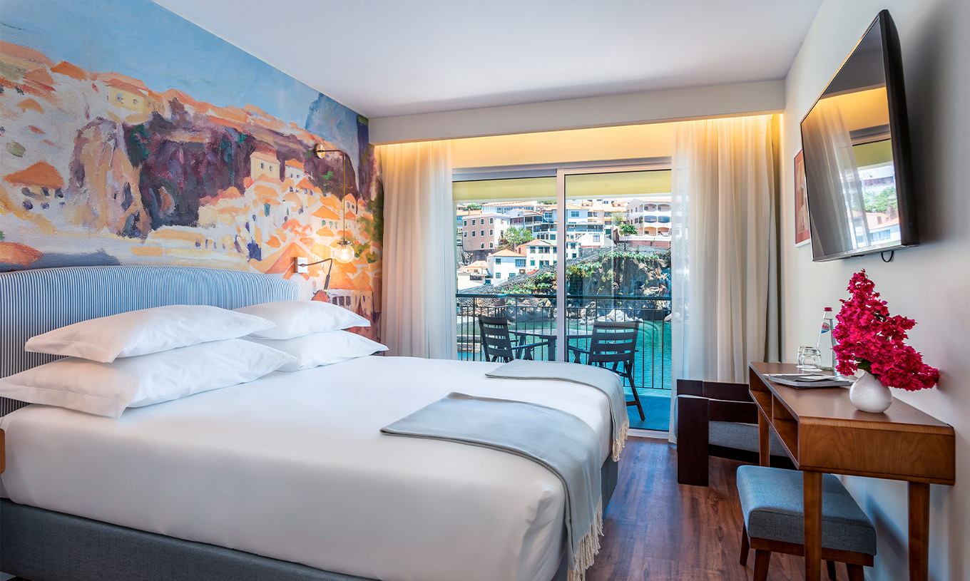 Das Deluxe Superior Bay View Zimmer im Pestana Churchill Bay hat blaue Töne, ein Doppelbett, einen Balkon und einen Sessel