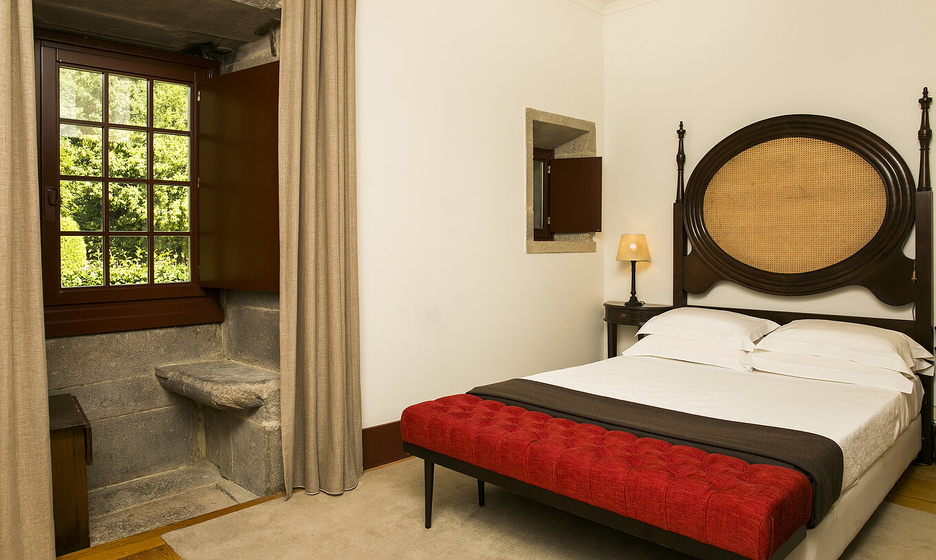Der klassische Raum der Pousada Mosteiro Guimarães hat ein Doppelbett mit einem Kopfteil aus dunklem Holz und einem Fenster