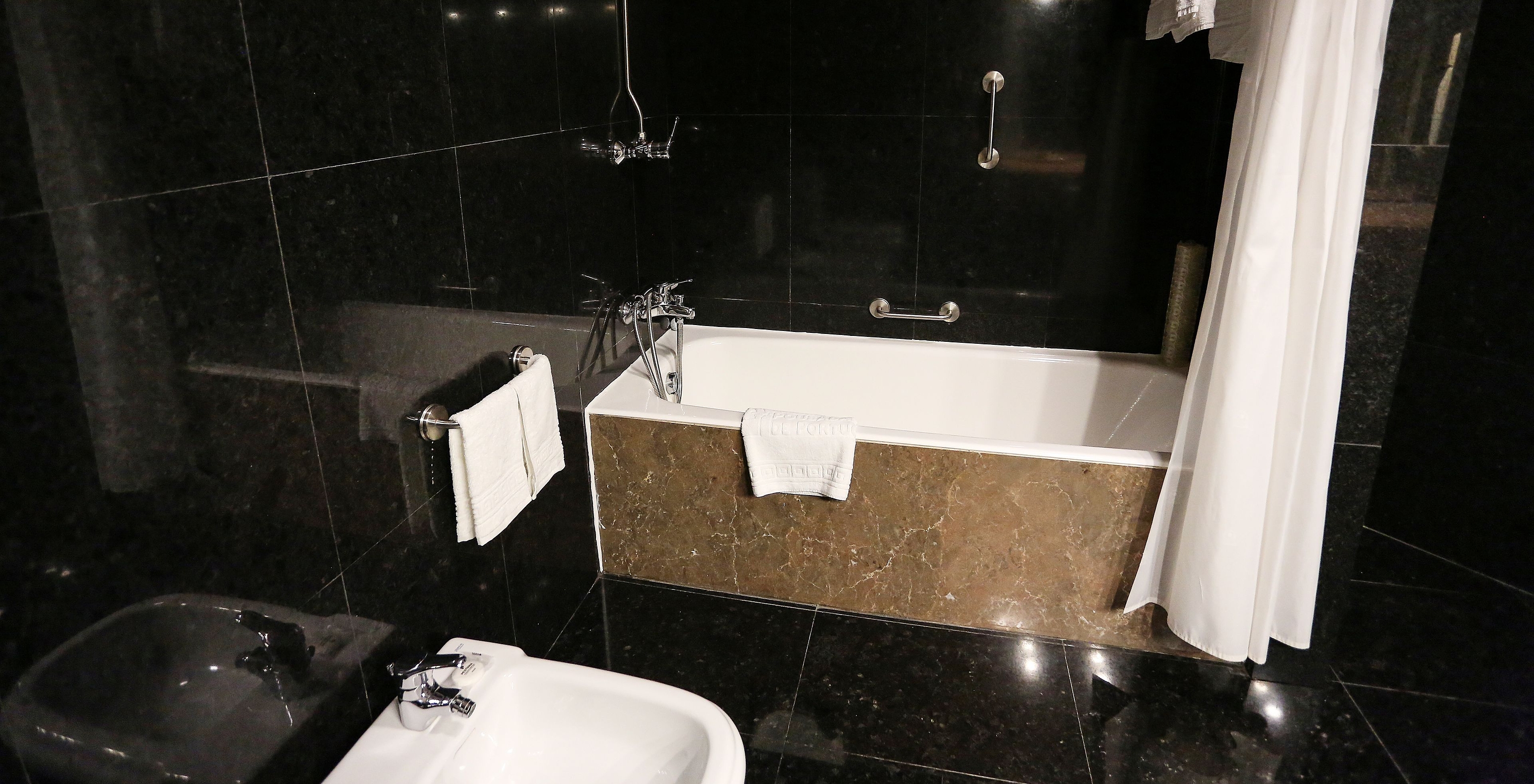 Die Large Family Suite der Pousada Valença hat ein dunkles Bad mit Badewanne und einem weißen Vorhang
