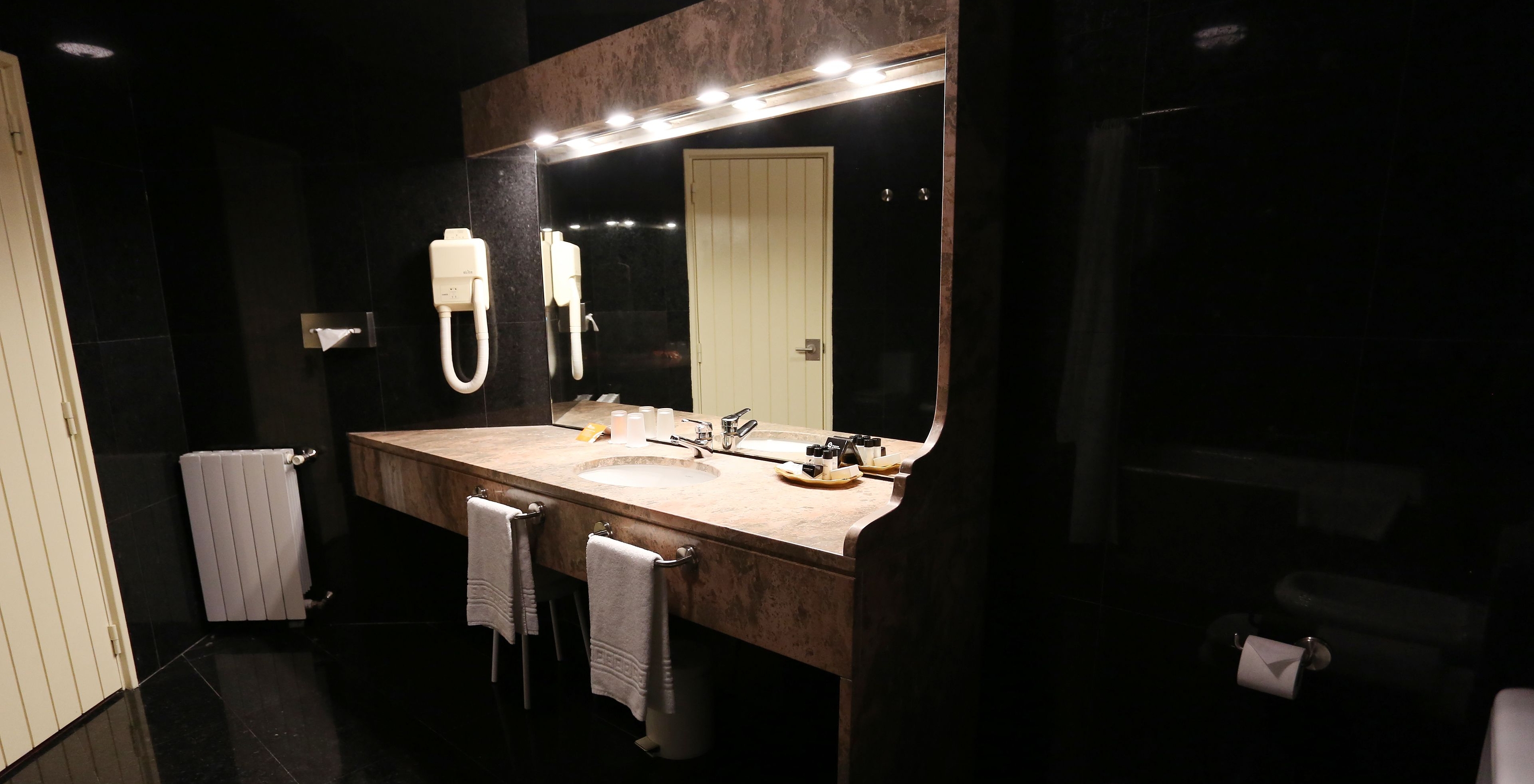 Die Junior Suite der Pousada Valença hat ein dunkles Bad mit Waschbecken, Handtüchern und WC