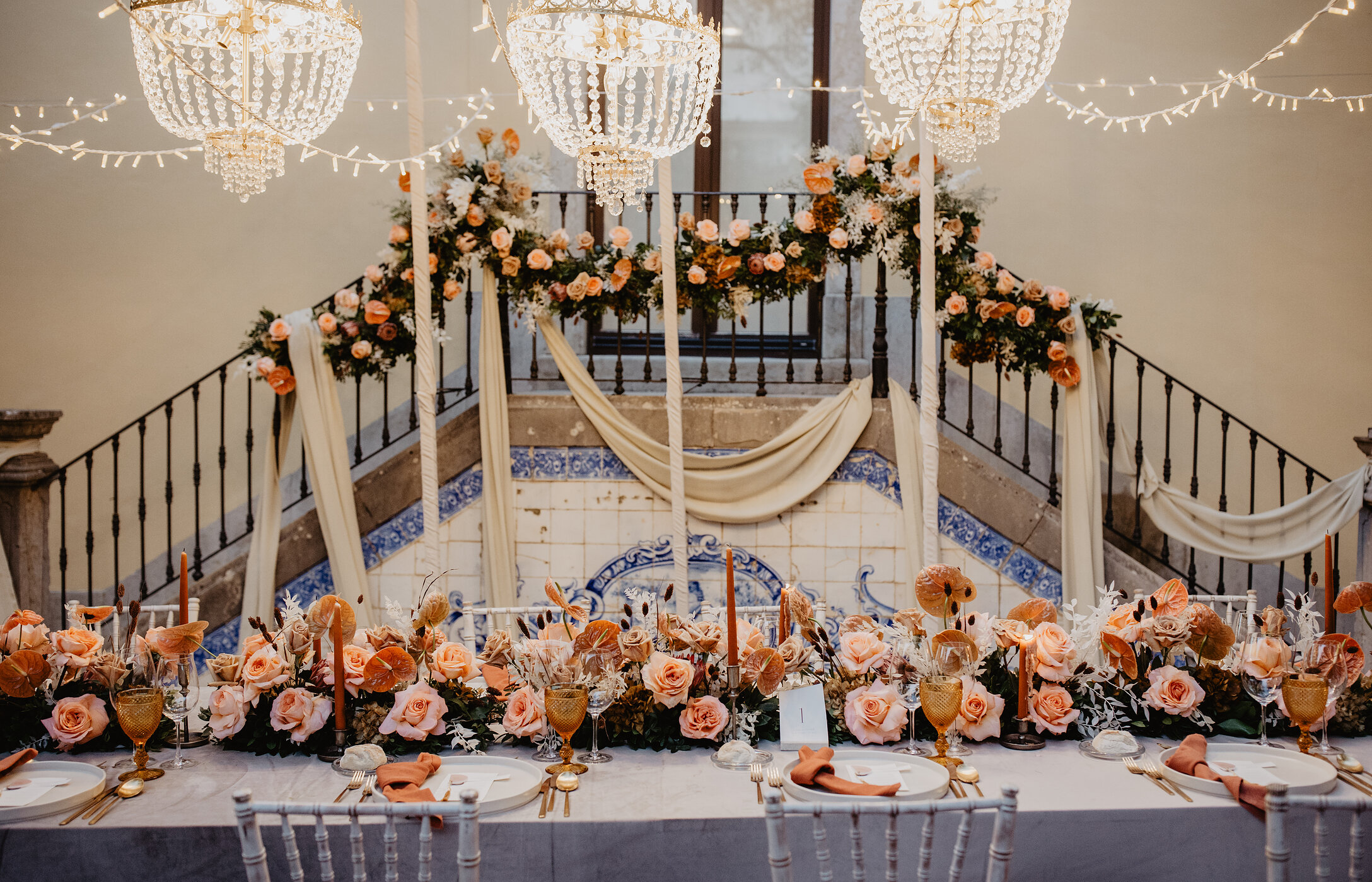 Hochzeit in einem historischen Raum, mit romantischer Deko, langer Tafel, Blumenarrangements aus Rosen und Kristallleuchtern
