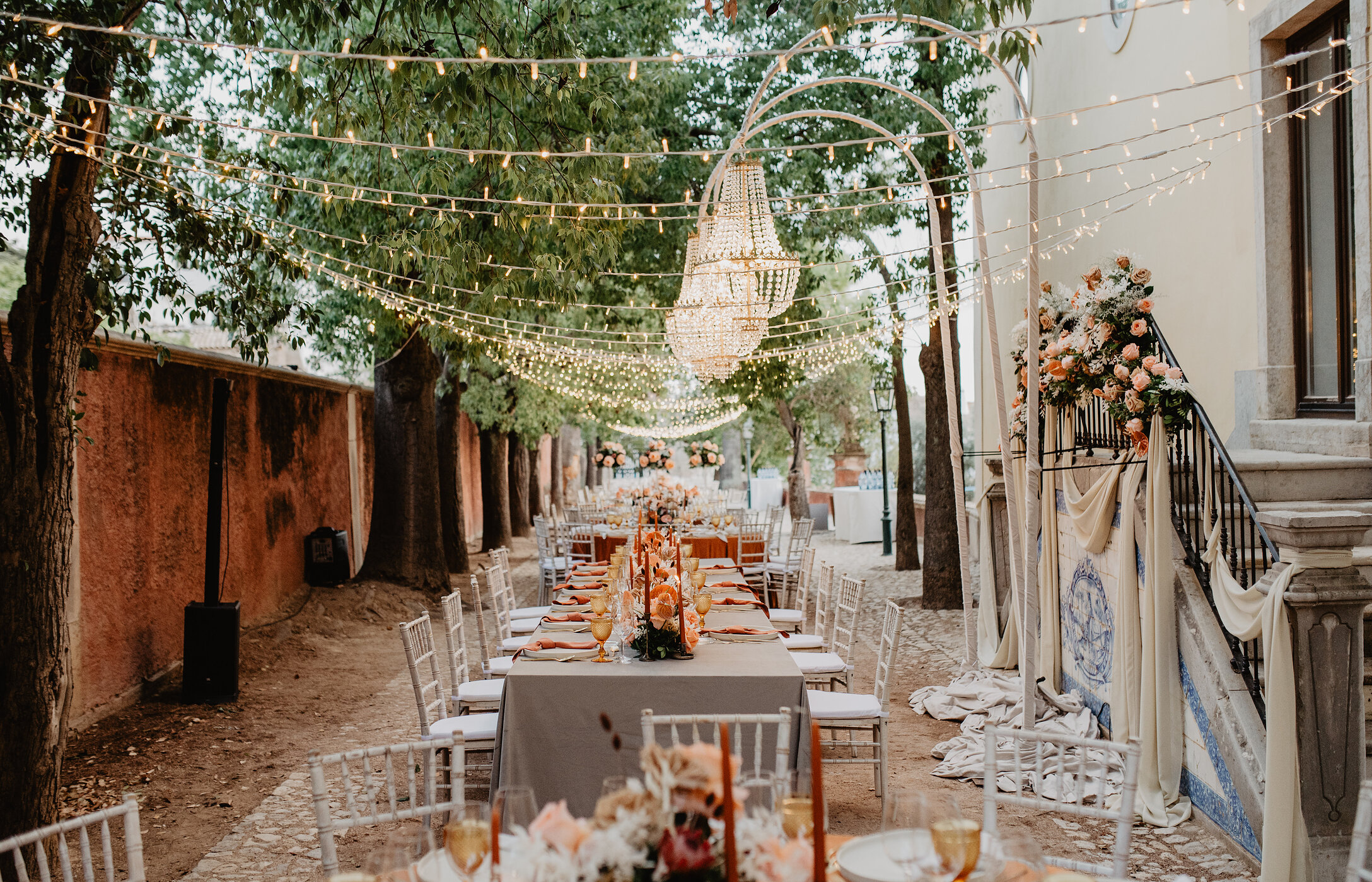 Hochzeit in einem historischen Außenbereich, mit elegant dekorierten Tischen und Beleuchtung, die an den Bäumen hängt