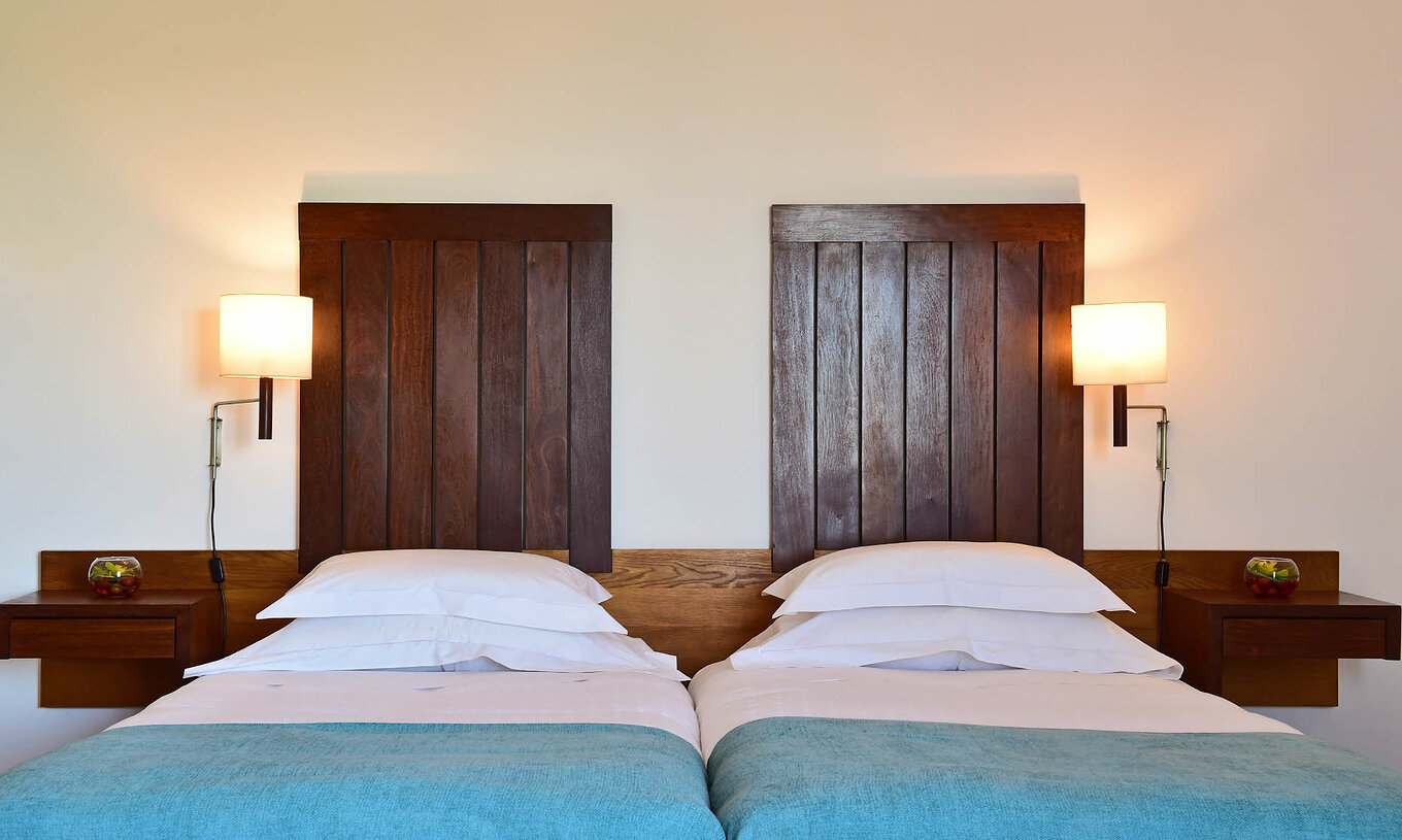 The Classic Family Room of the Pousada Castelo Alcácer do Sal has two beds, with a blue blanket and a wooden headboard