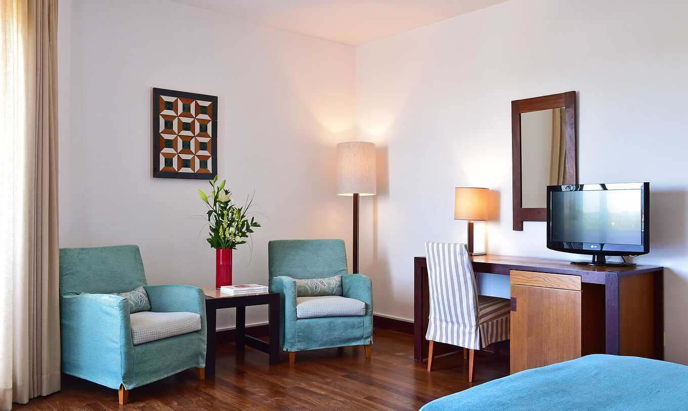 The Classic Family Room of the Pousada Castelo Alcácer do Sal has a desk with a television and two blue armchairs