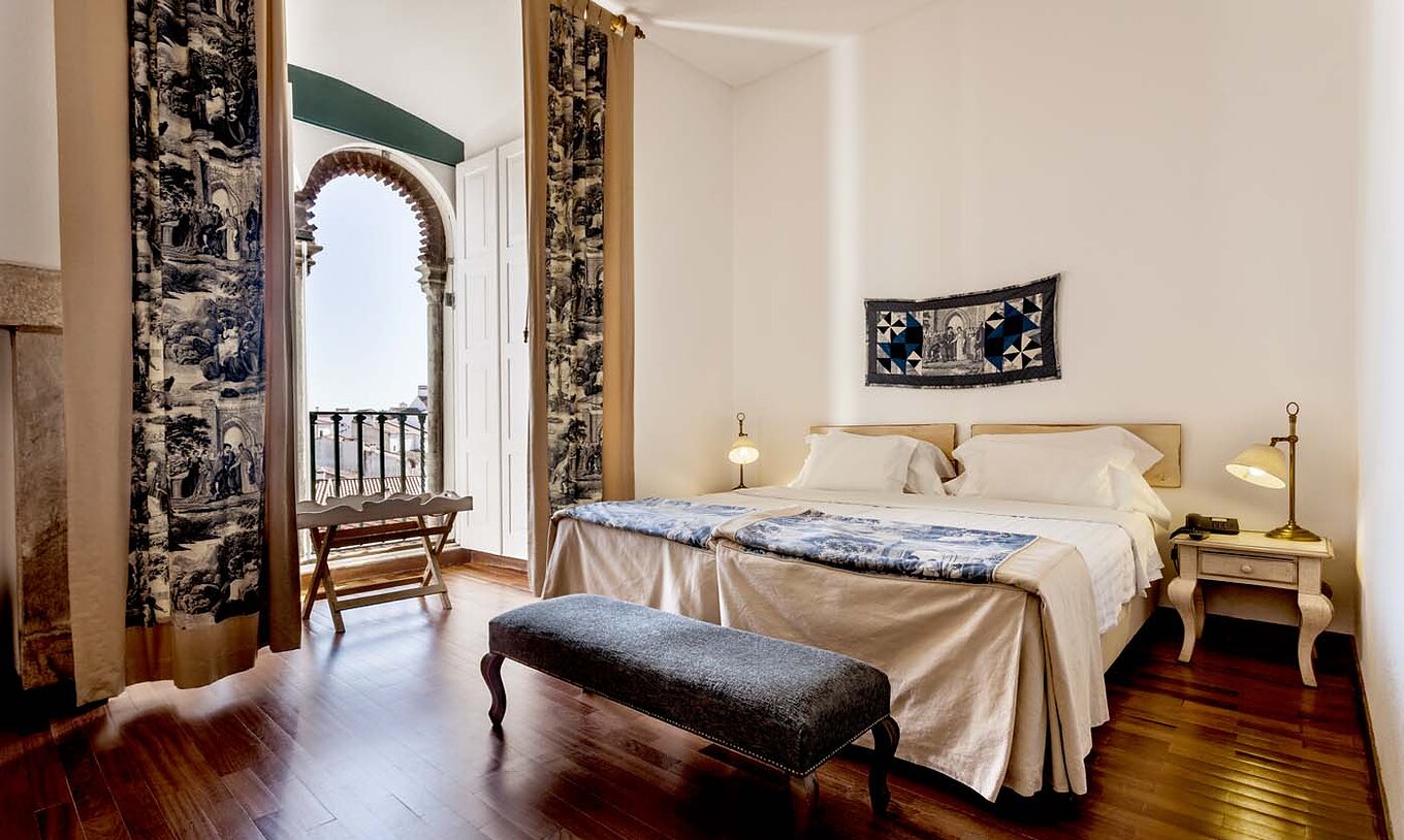 The Superior Room of the Pousada Castelo Alvito has two beds, two bedside tables, and a window with shutters and curtains