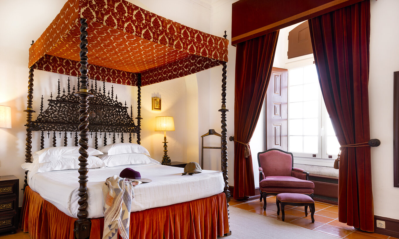 The Junior Suite at Pousada Castelo Estremoz has an antique double bed with a canopy covered by fabric and dark wood