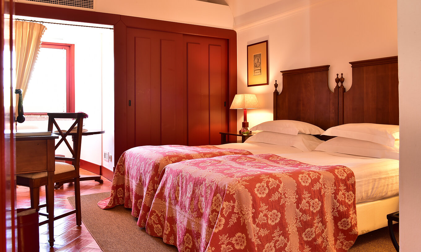 The Classic Room of The Pousada Convento Beja has two joined beds with a red bedspread, a window, and wardrobes