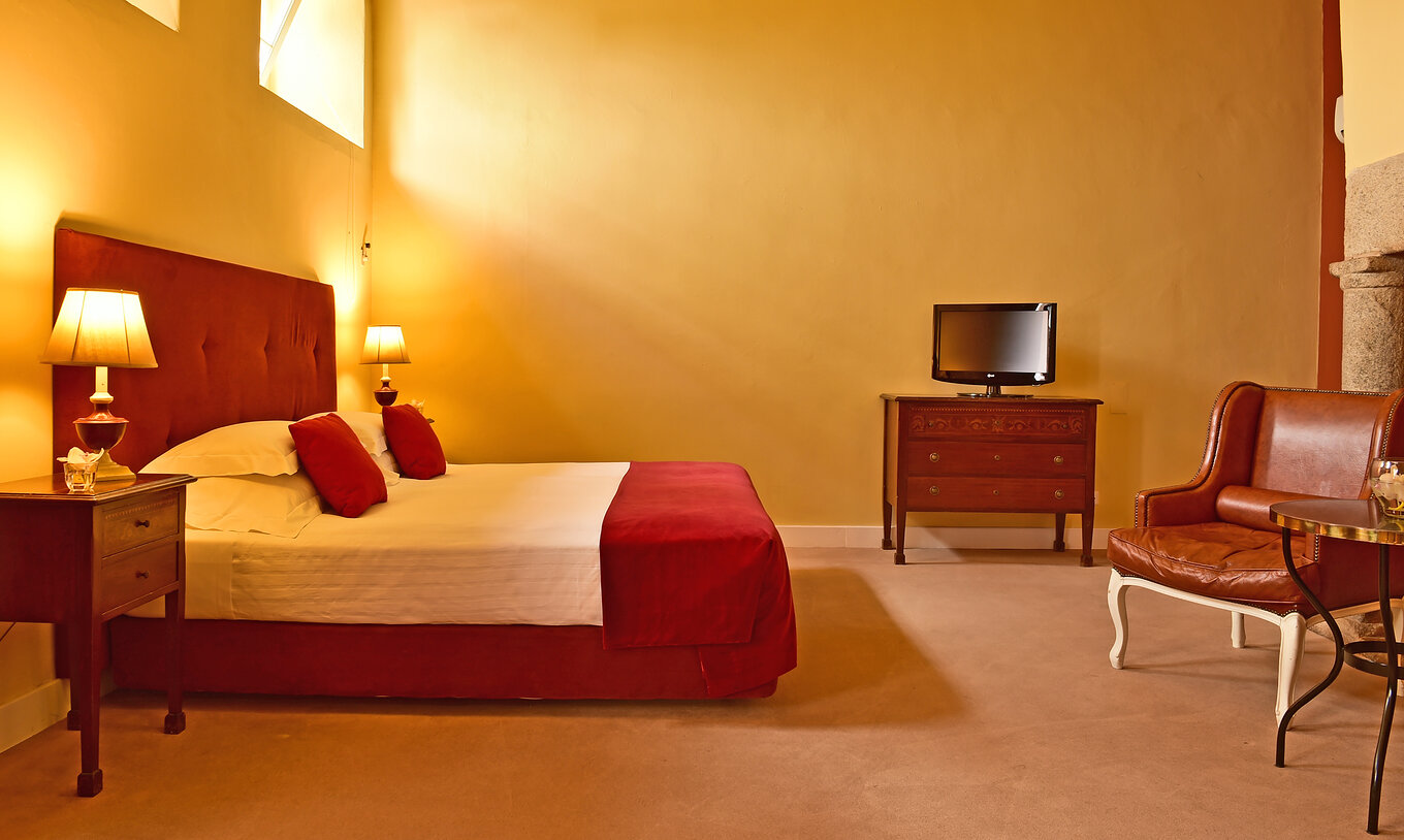 The Superior Family of The Pousada Convento Évora has a double bed in red tones, a television, and an armchair