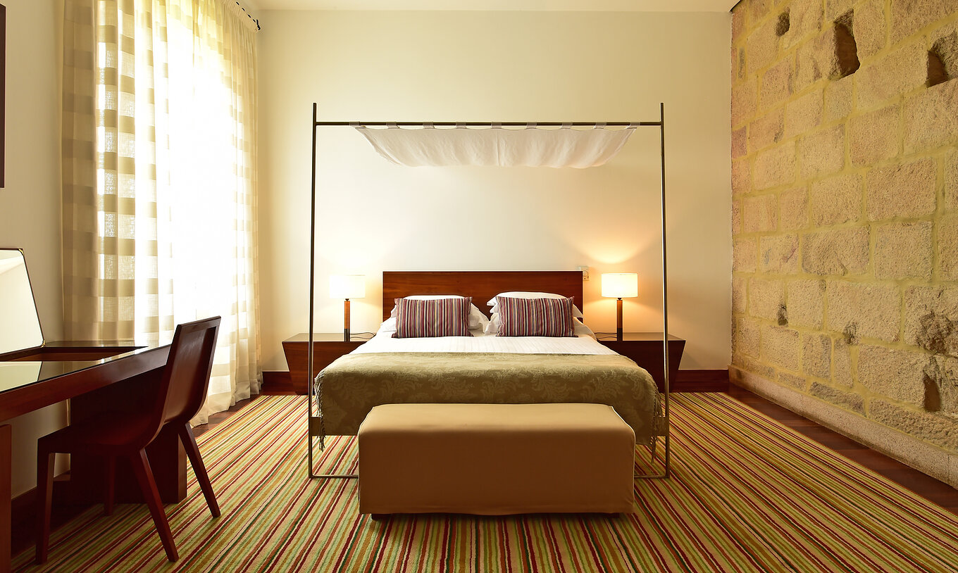 The Historical Superior Room of The Pousada Mosteiro Crato has stone walls with a four-poster double bed and a stool