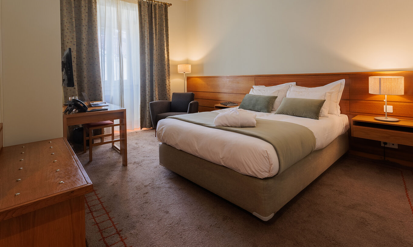 The Family Room of The Pousada Ourém features a double bed with a bathrobe on top and a television