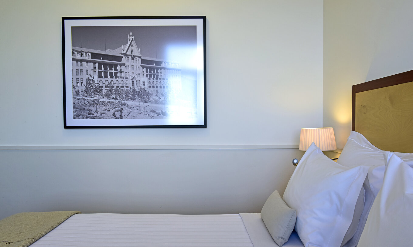 The Classic Family Room of The Serra da Estrela Inn has a double bed with a wooden headboard and a painting of the sanatorium