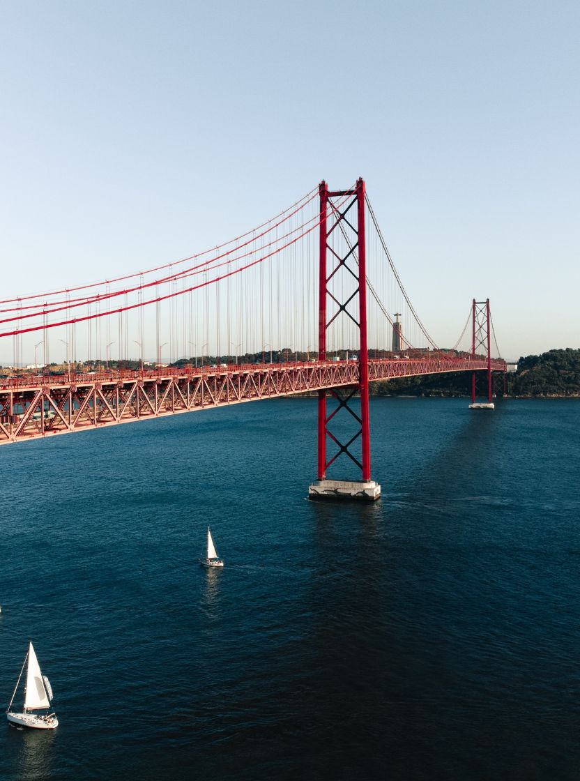Panoramic view of the city of Lisbon, with the Tejo River featuring several boats and the 25 de Abril Bridge