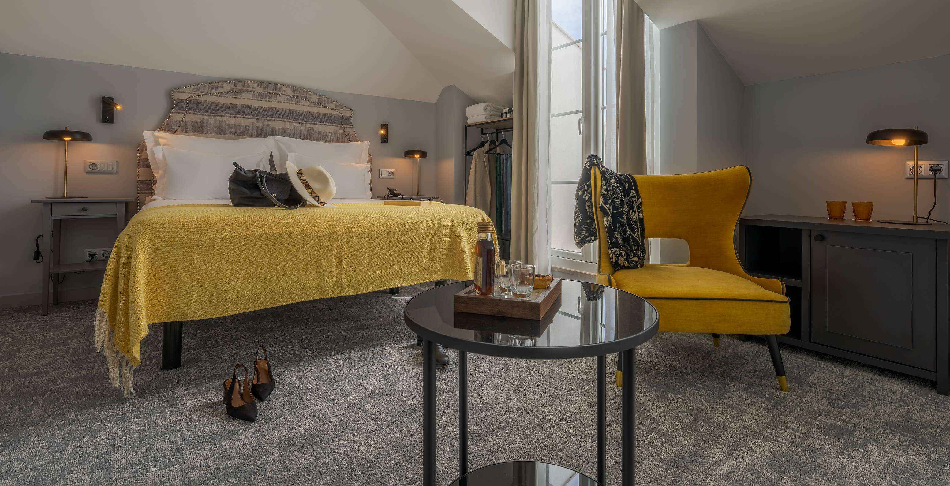The Junior Suite at Pousada Alfama offers a double bed with a yellow throw blanket, a small table, and a yellow armchair