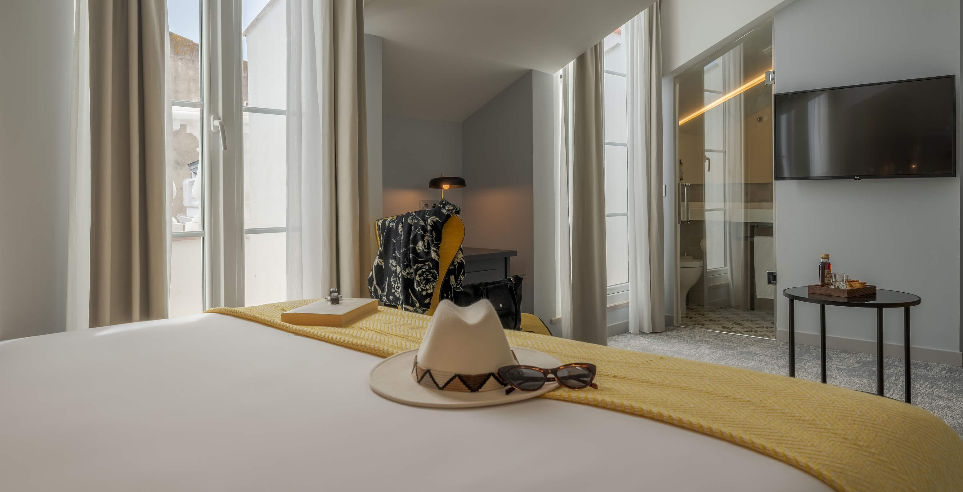 The Junior Suite at Pousada Alfama has two large windows, a TV, and a bathroom with a transparent door