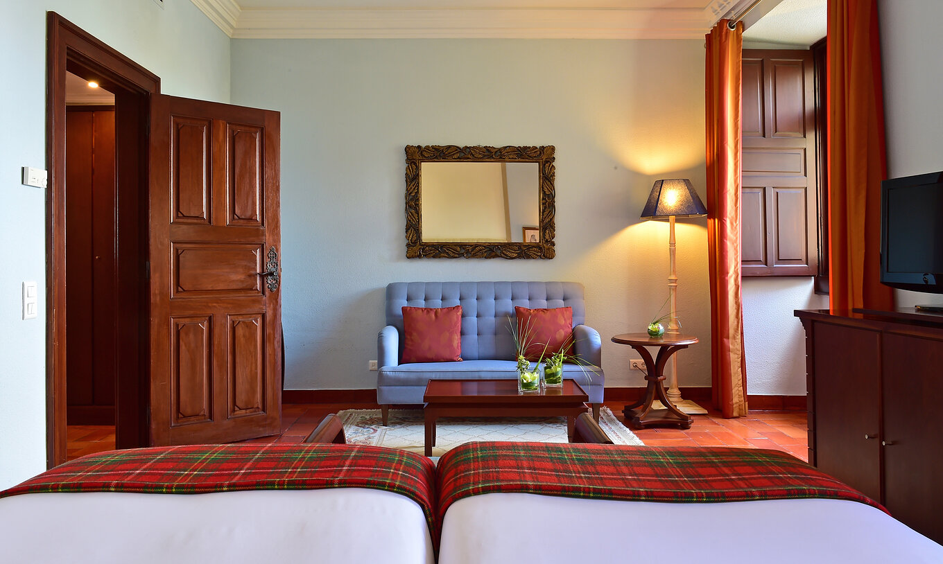 The Classic Family Room at Pousada Castelo Palmela has two beds, a blue sofa with a small table, and a window