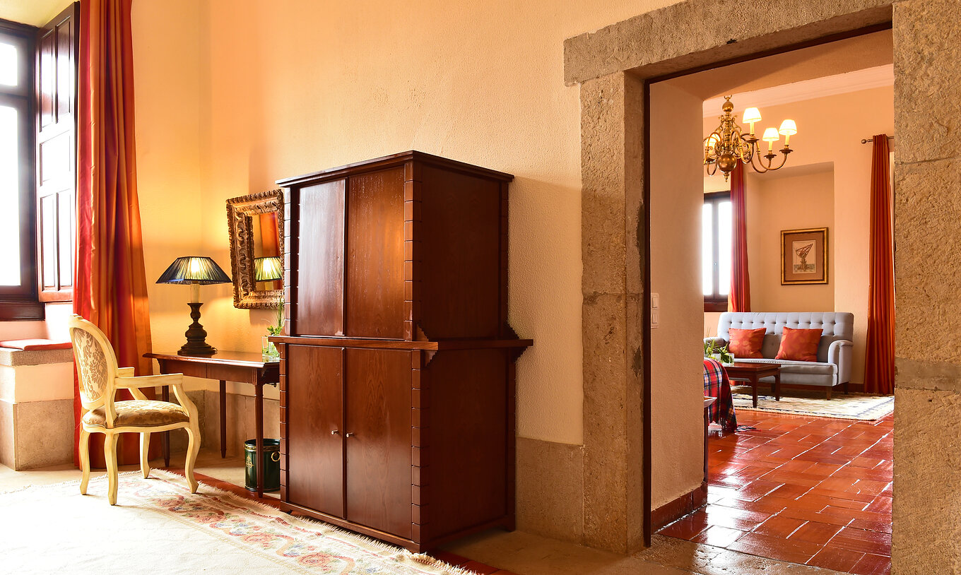 The Master Suite at Pousada Castelo Palmela has a living room with a desk with a chair, solid wood furniture, and a window